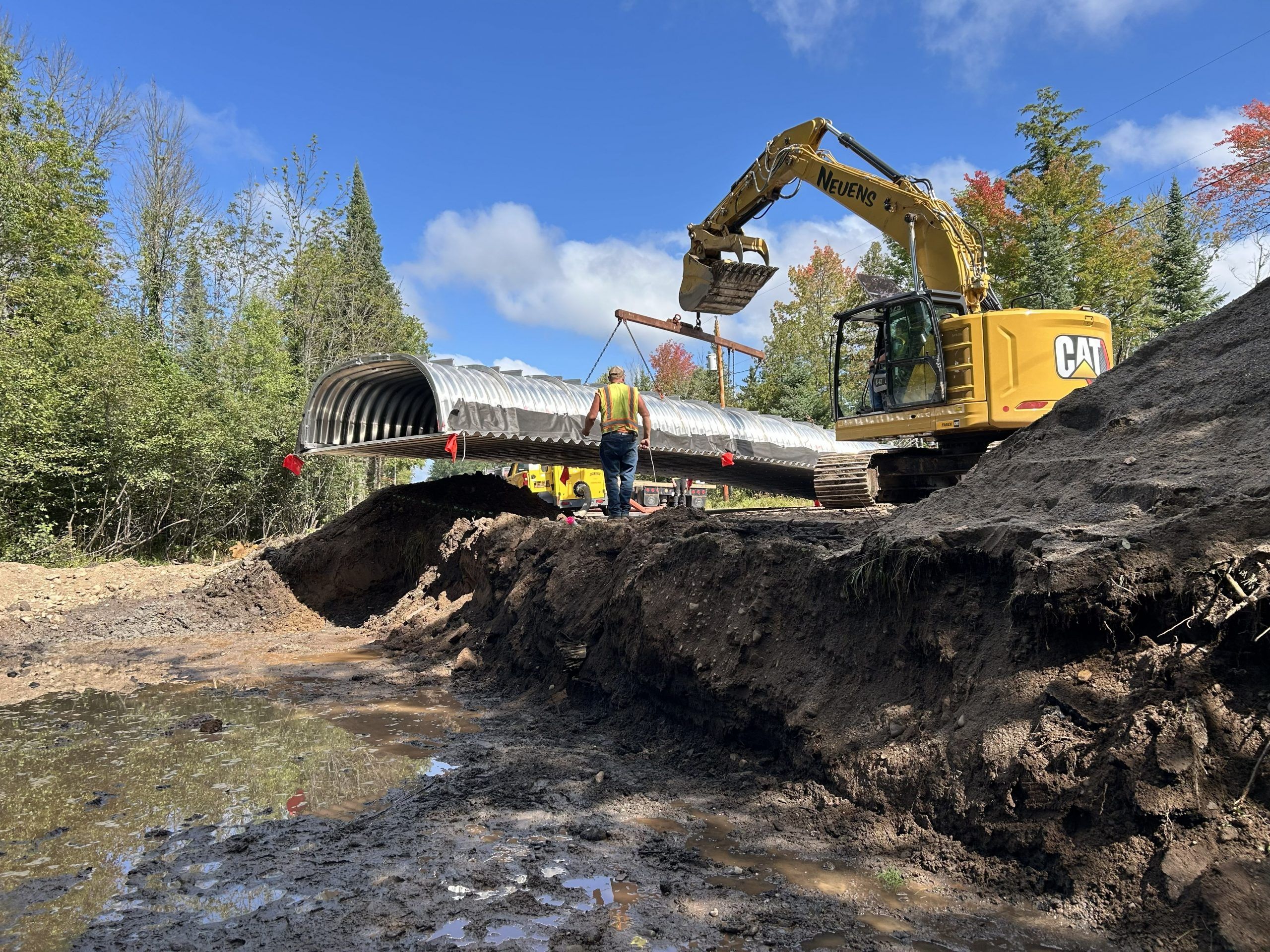 An excavator lowers an aluminum culvert into place on Trybom Dr.